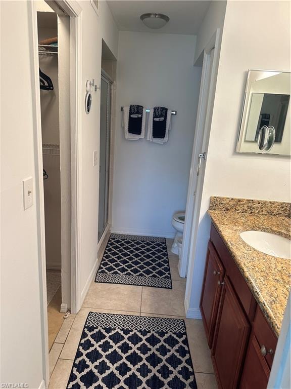 Bathroom with an enclosed shower, vanity, tile patterned flooring, and toilet