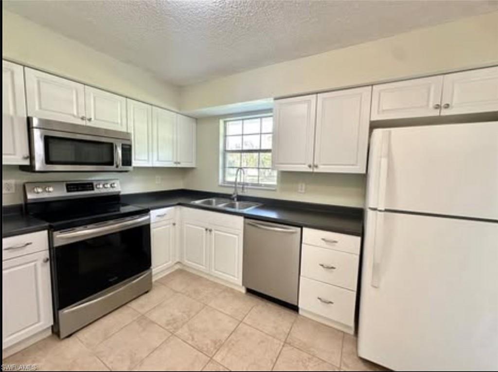 Kitchen featuring appliances with stainless steel finishes, a textured ceiling, white cabinetry, dark countertops, and light tile patterned floors