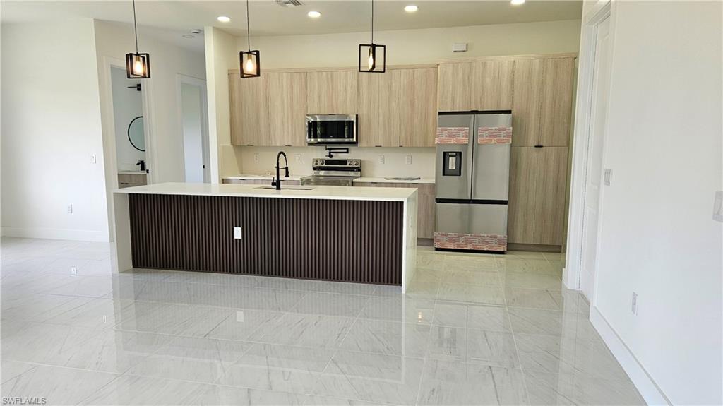 Kitchen with light brown cabinets, hanging light fixtures, appliances with stainless steel finishes, recessed lighting, and light stone counters