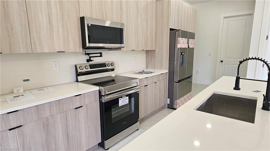 Kitchen with modern cabinets, light brown cabinetry, stainless steel appliances, and light tile patterned floors