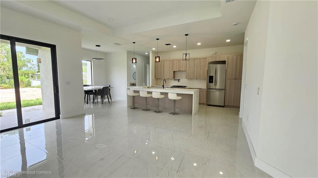 Kitchen with recessed lighting, decorative light fixtures, a kitchen bar, stainless steel fridge, and a center island with sink