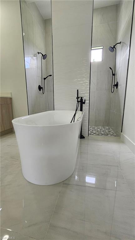 Bathroom featuring a walk in shower, a soaking tub, and light marble finish floors