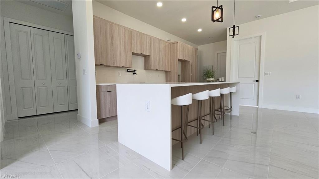 Kitchen featuring light brown cabinetry, modern cabinets, recessed lighting, a breakfast bar, and decorative light fixtures