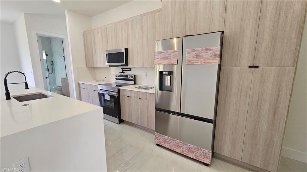 Kitchen featuring appliances with stainless steel finishes, modern cabinets, light stone counters, and light brown cabinetry