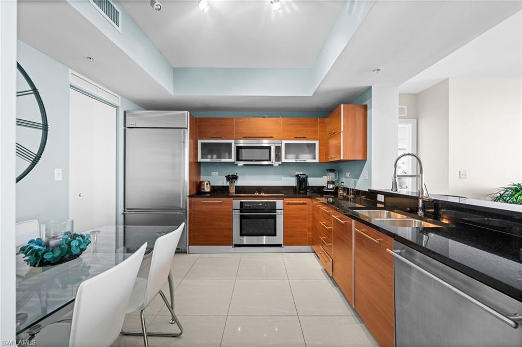 Kitchen featuring brown cabinetry, dark stone counters, modern cabinets, stainless steel appliances, and light tile patterned floors
