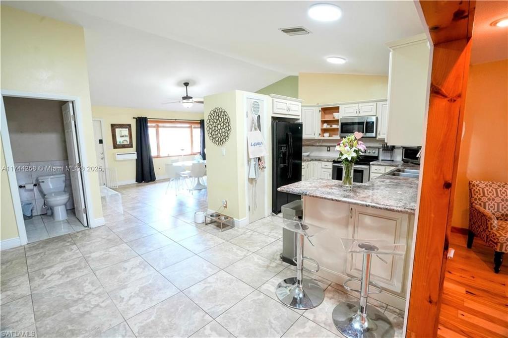 Kitchen with a peninsula, lofted ceiling, open shelves, appliances with stainless steel finishes, and ceiling fan