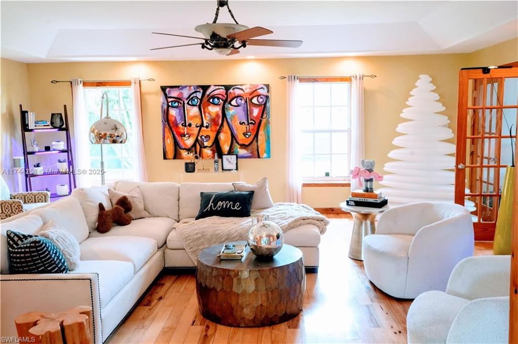 Living room featuring a tray ceiling, wood finished floors, and ceiling fan