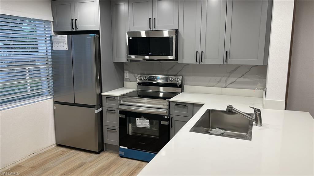 Kitchen featuring gray cabinets, stainless steel appliances, light wood finished floors, and tasteful backsplash