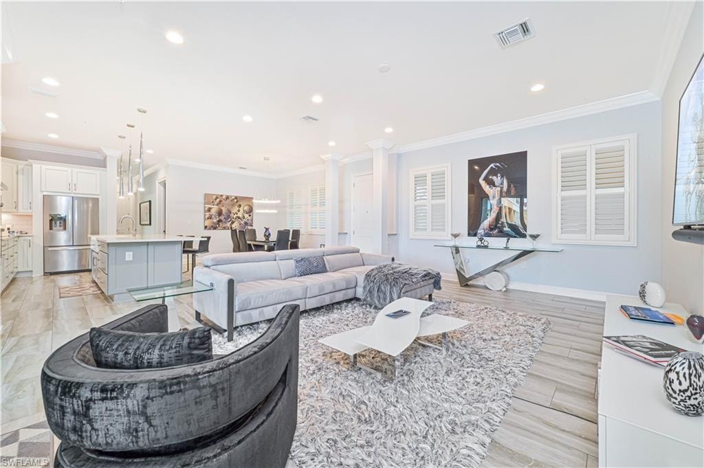 Living area with ornamental molding, ornate columns, recessed lighting, and light wood-style floors