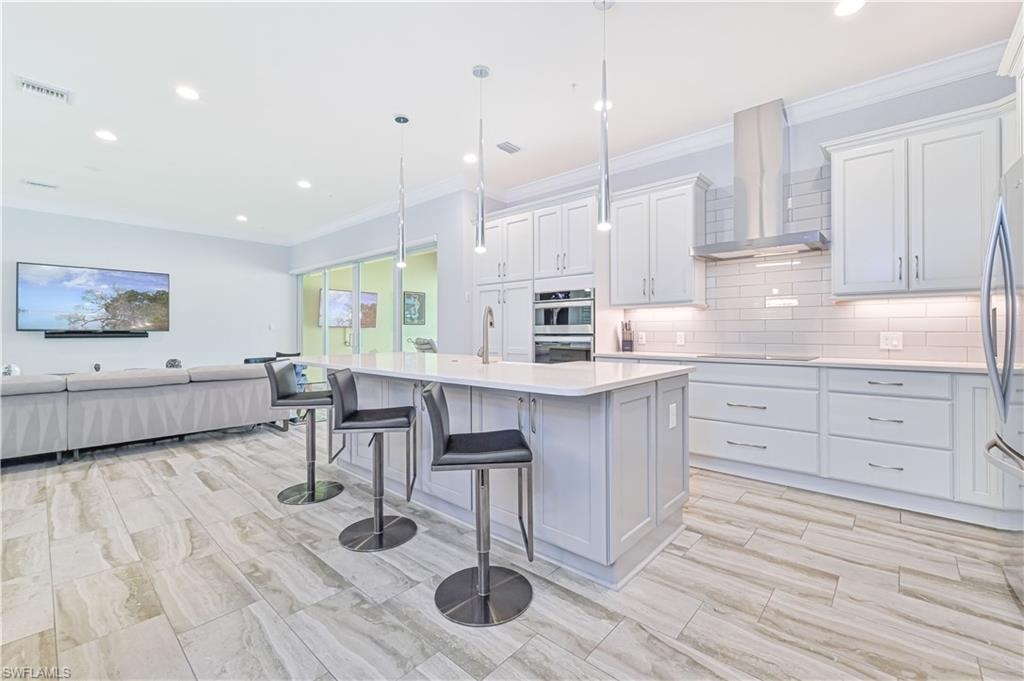 Kitchen with decorative light fixtures, crown molding, white cabinets, appliances with stainless steel finishes, and a kitchen island with sink