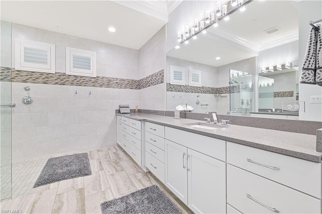 Full bathroom with tile walls, walk in shower, vanity, crown molding, and recessed lighting