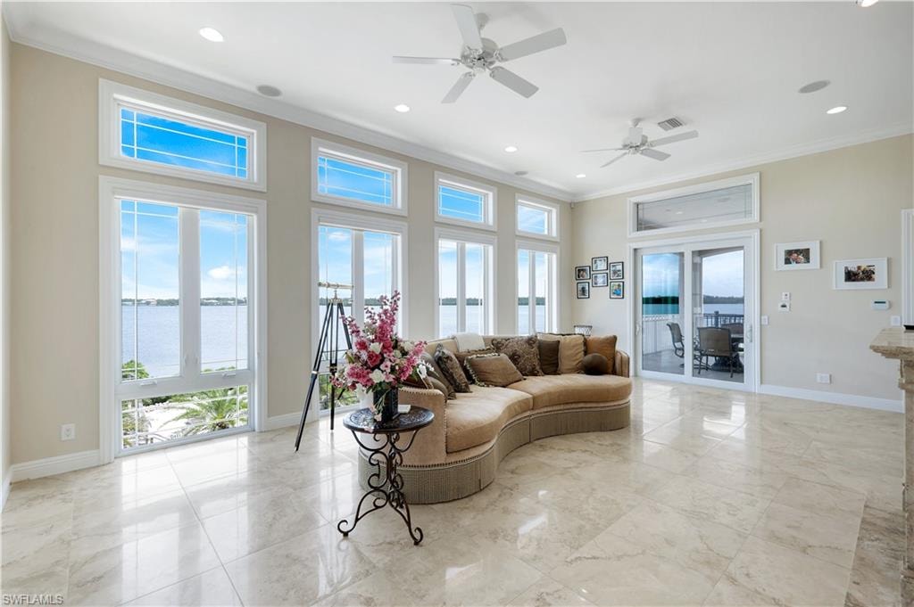 Living area off the primary bedroom featuring crown molding, a water view, light marble finish floors, a ceiling fan, and recessed lighting