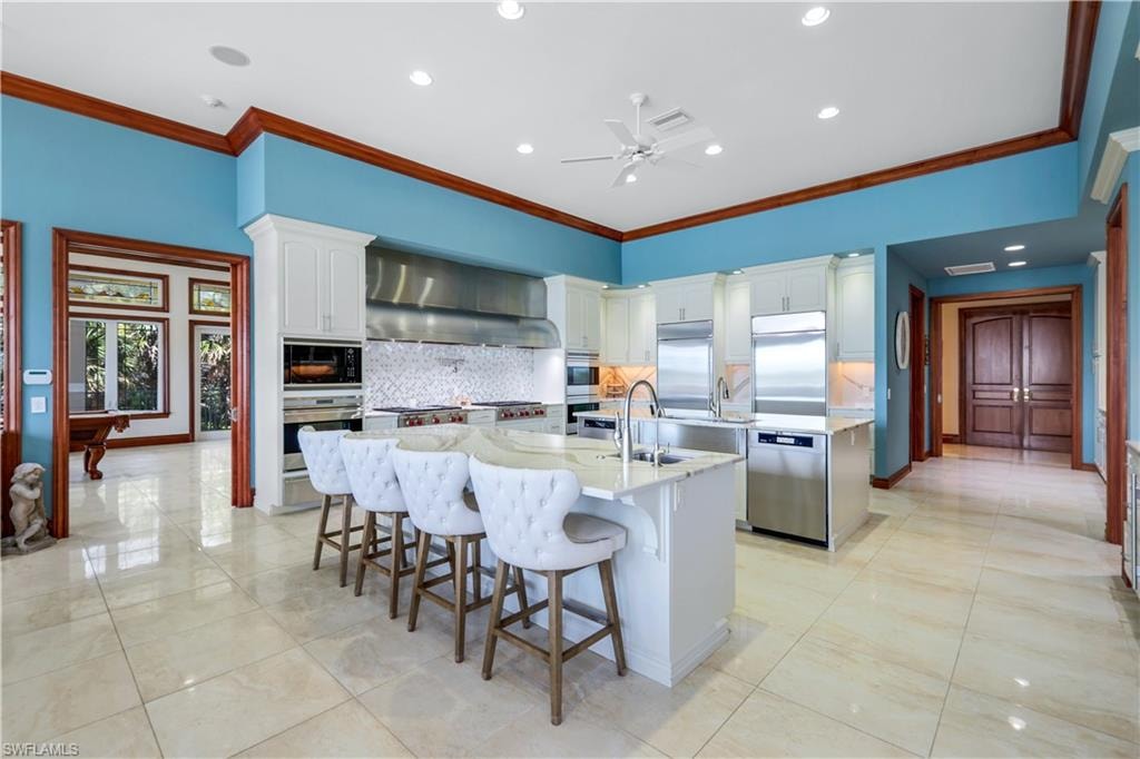 Kitchen featuring crown molding, decorative backsplash, a kitchen breakfast bar, white cabinets, and recessed lighting