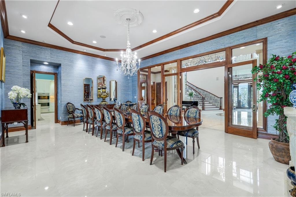 Dining area with wallpapered walls, a raised ceiling, stairway, ornamental molding, and a chandelier