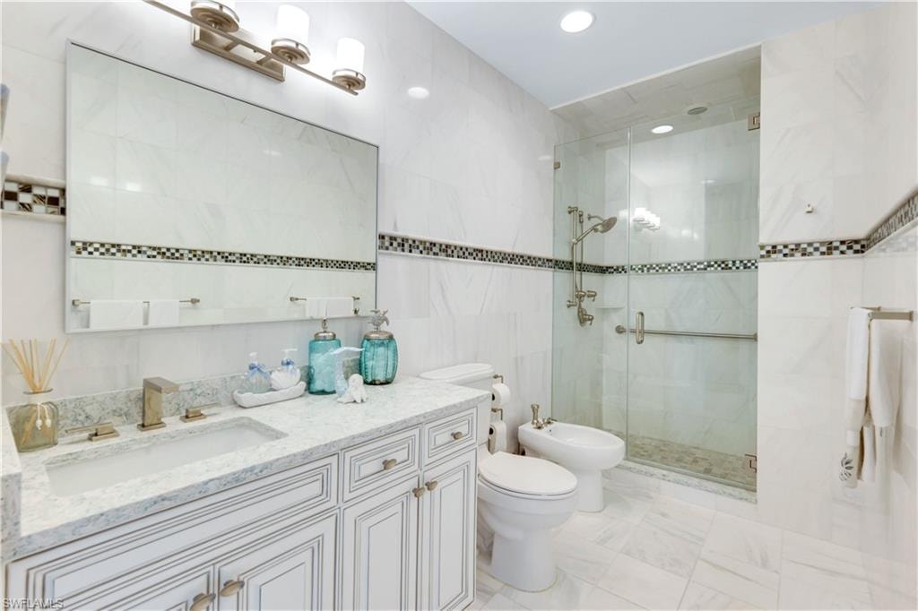 Full bath with tile walls, a bidet, vanity, a stall shower, and recessed lighting