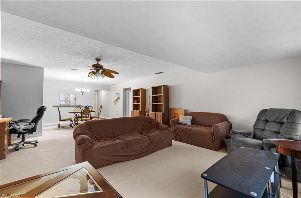 Living room with carpet flooring, a desk, ceiling fan, a textured ceiling, and a chandelier