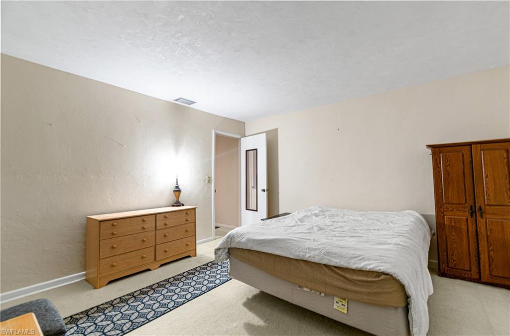 Bedroom with a textured wall, light carpet, and a textured ceiling