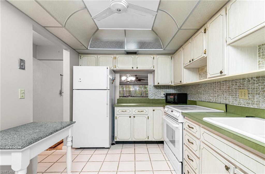 Kitchen featuring white appliances, light tile patterned floors, a ceiling fan, backsplash, and white cabinets