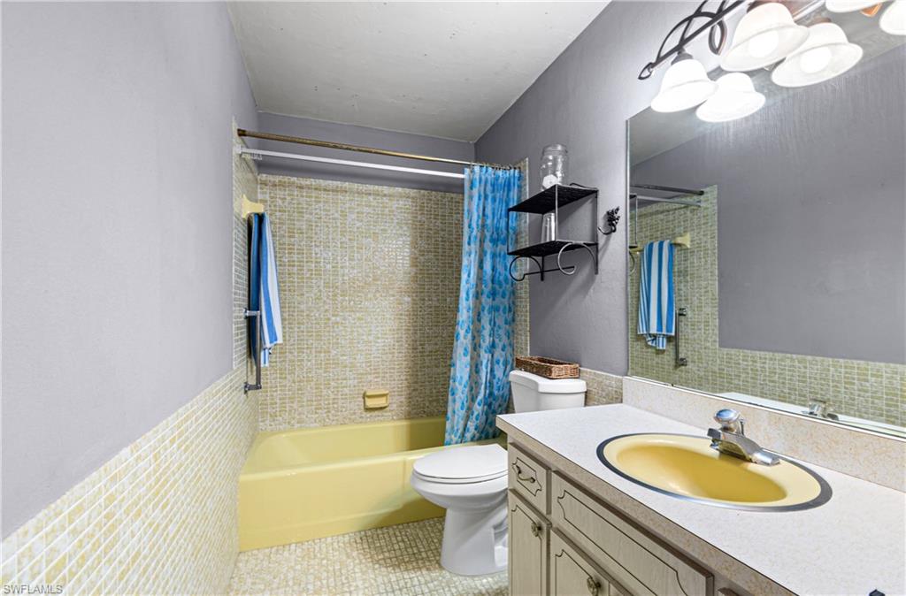 Full bathroom with shower / bath combo, vanity, light tile patterned floors, and wainscoting