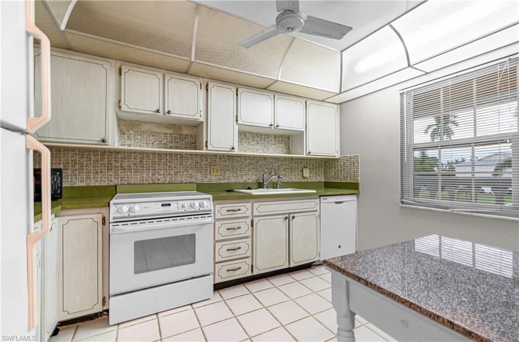 Kitchen featuring white appliances, backsplash, a ceiling fan, light tile patterned floors, and white cabinetry