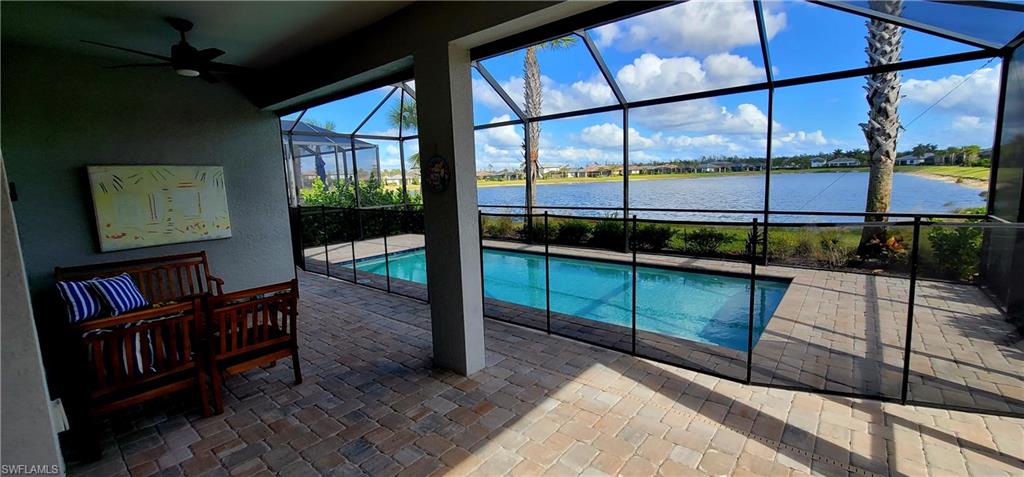 View of pool with glass enclosure, ceiling fan, a water view, and a patio