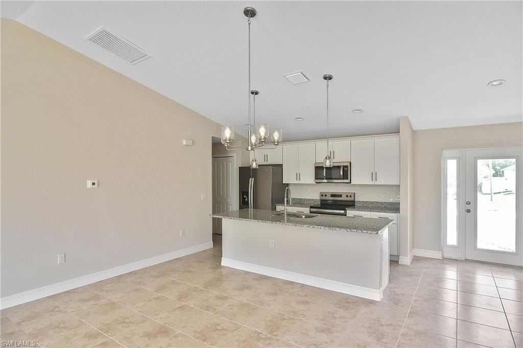 Kitchen with pendant lighting, dark stone countertops, stainless steel appliances, an island with sink, and white cabinetry