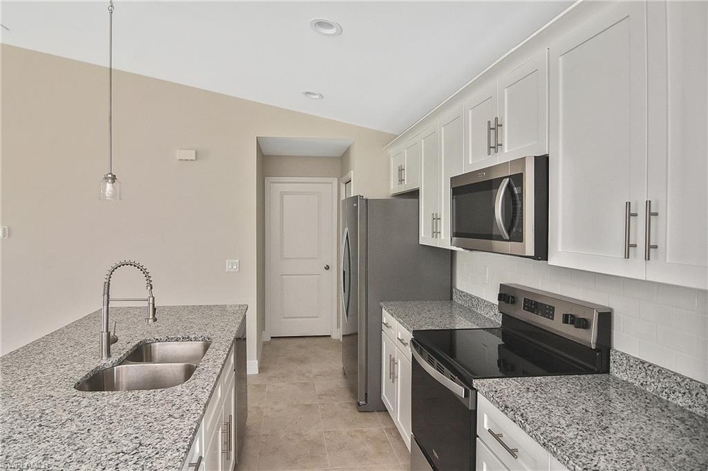 Kitchen featuring stainless steel appliances, hanging light fixtures, light stone countertops, white cabinets, and lofted ceiling