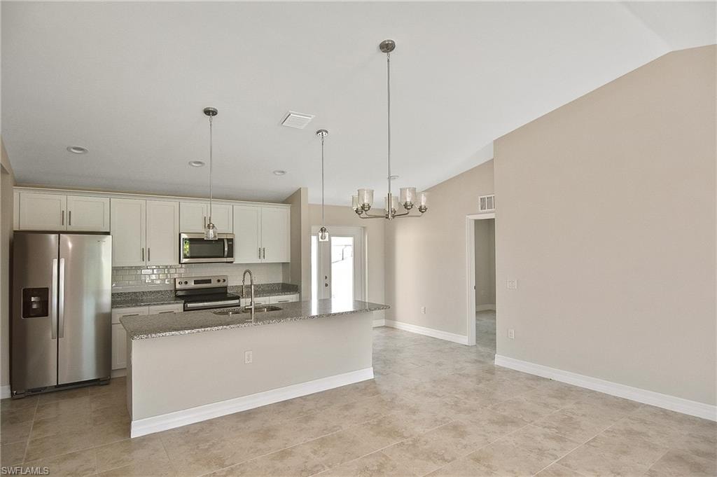 Kitchen with appliances with stainless steel finishes, decorative light fixtures, light stone counters, backsplash, and a chandelier