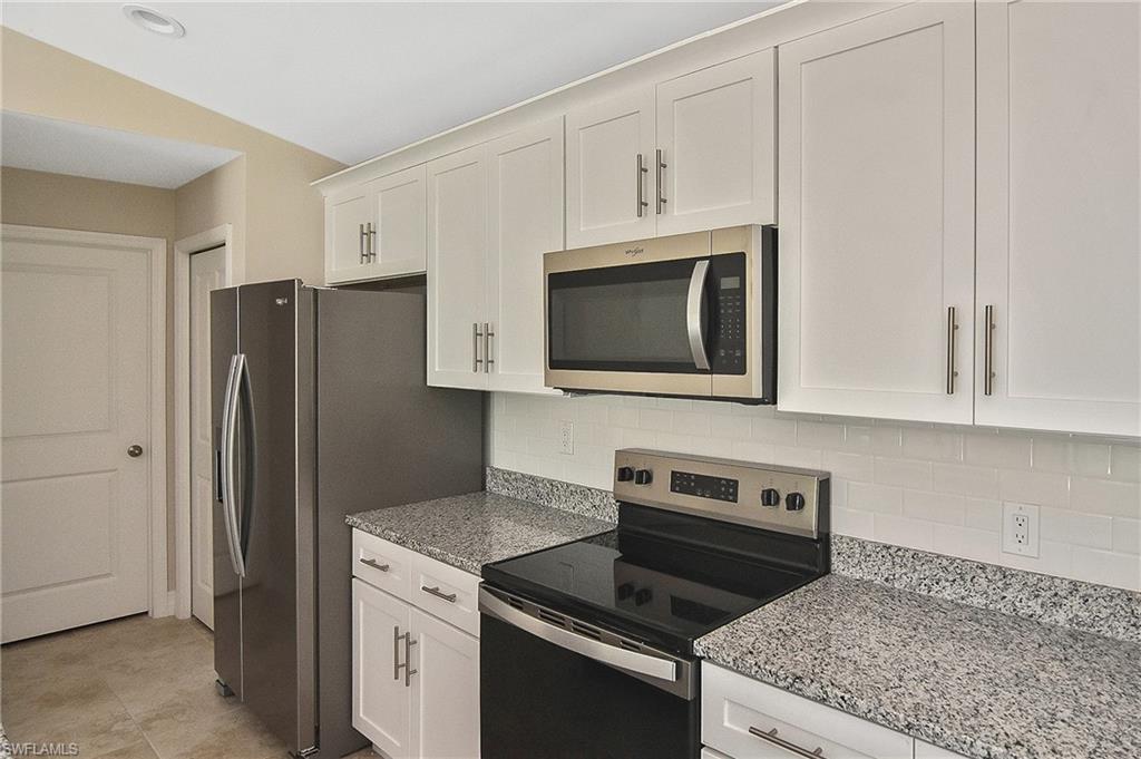 Kitchen with stainless steel appliances, backsplash, light stone countertops, and white cabinetry
