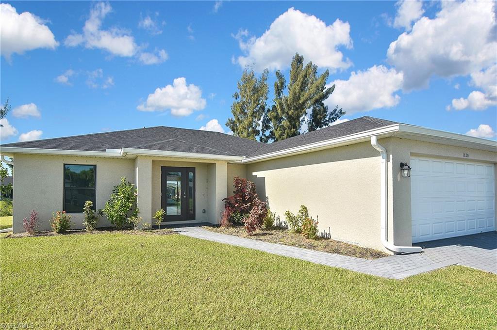 Ranch-style home featuring a front lawn, stucco siding, a garage, driveway, and a shingled roof