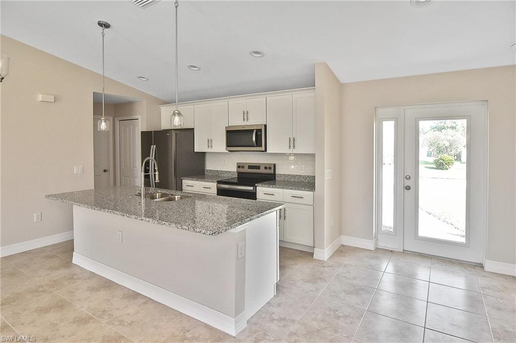 Kitchen with appliances with stainless steel finishes, light stone counters, decorative backsplash, a kitchen island with sink, and pendant lighting
