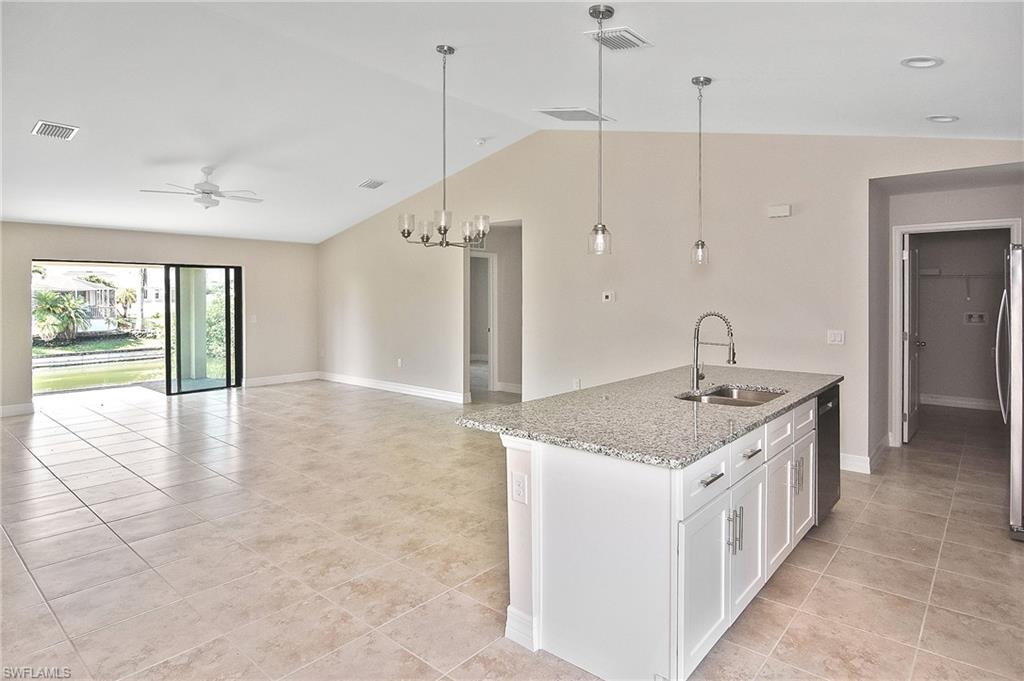 Kitchen with hanging light fixtures, light stone counters, white cabinetry, a kitchen island with sink, and vaulted ceiling