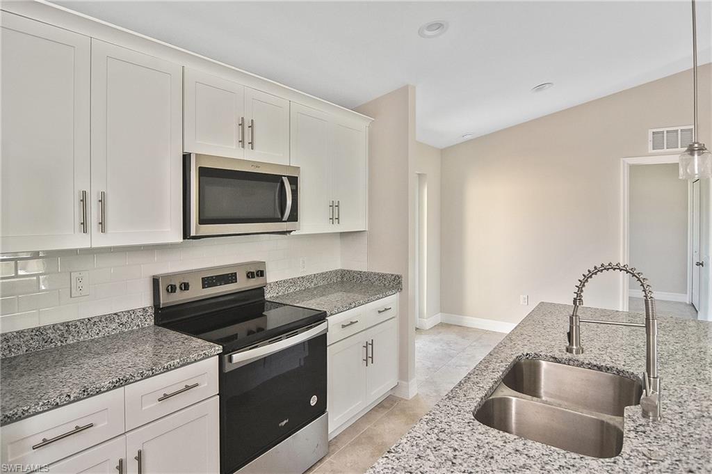 Kitchen with appliances with stainless steel finishes, white cabinetry, light stone counters, pendant lighting, and recessed lighting