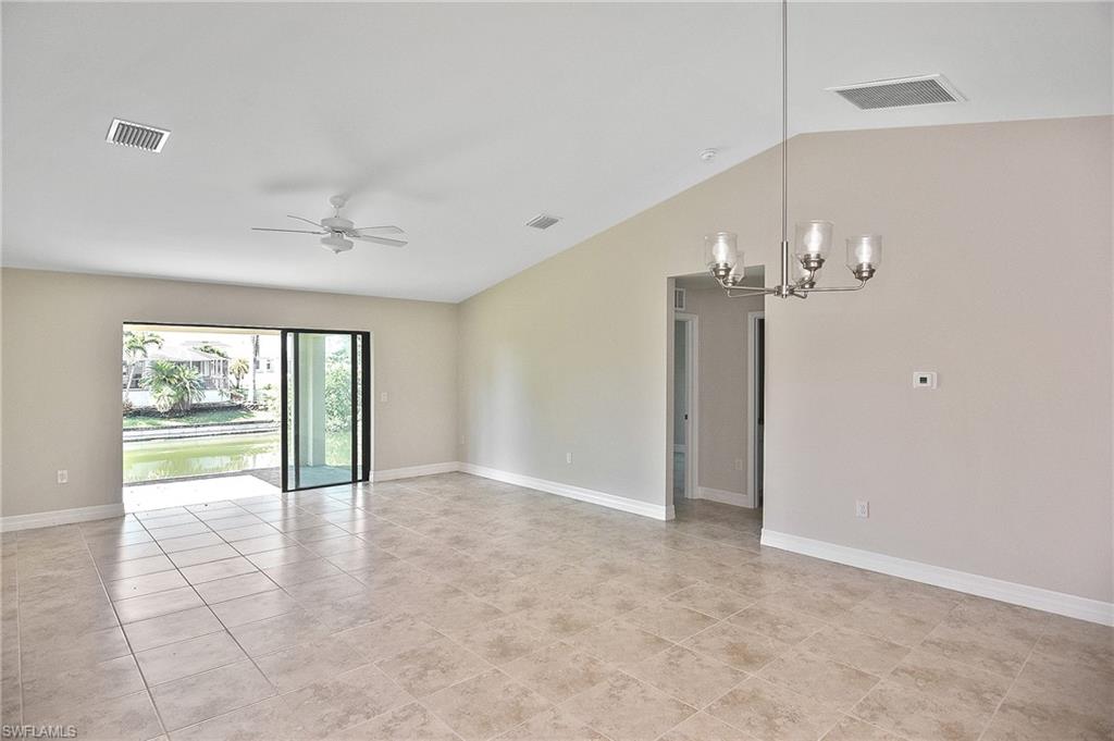 Empty room featuring vaulted ceiling, a chandelier, ceiling fan, and light tile patterned floors