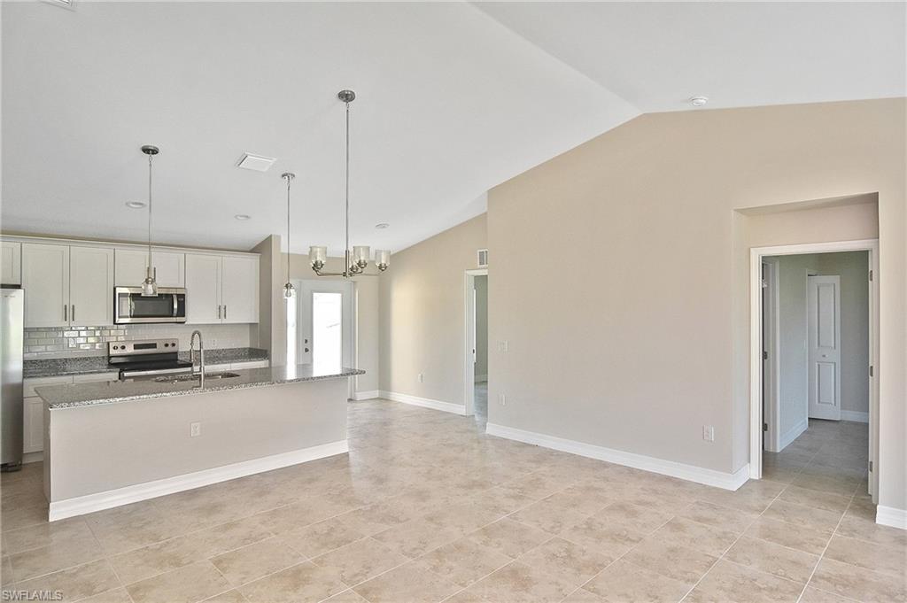Kitchen featuring hanging light fixtures, tasteful backsplash, dark stone countertops, appliances with stainless steel finishes, and a kitchen island with sink