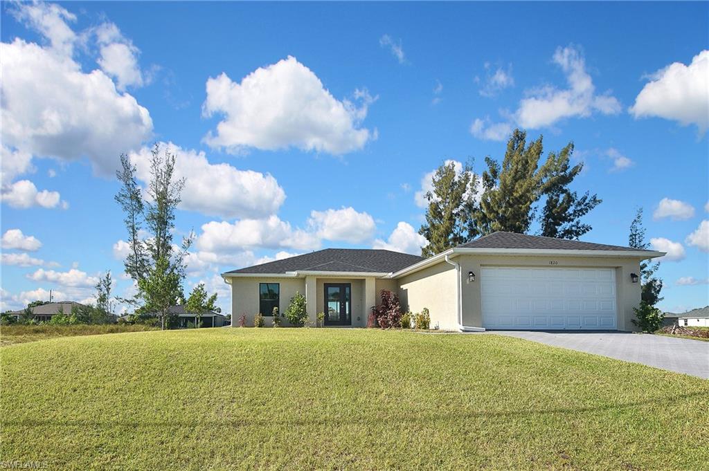 View of front of property with a front yard, driveway, an attached garage, and stucco siding