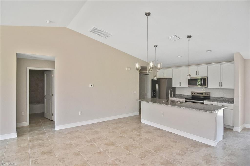 Kitchen with pendant lighting, vaulted ceiling, tasteful backsplash, stainless steel appliances, and dark stone countertops