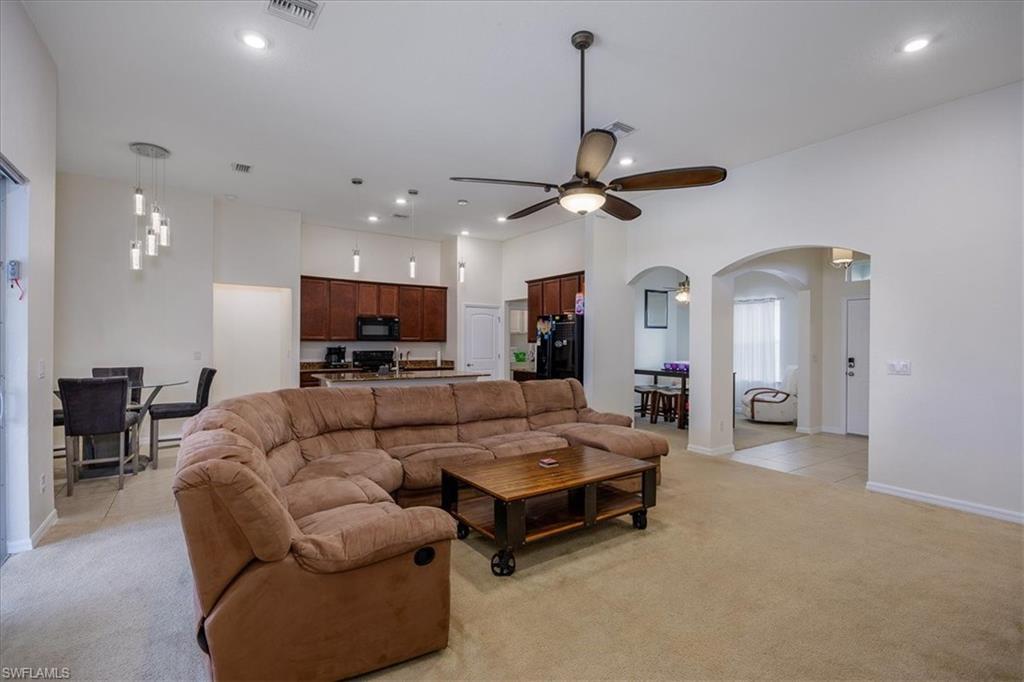 Living room with a ceiling fan, light carpet, arched walkways, recessed lighting, and a towering ceiling