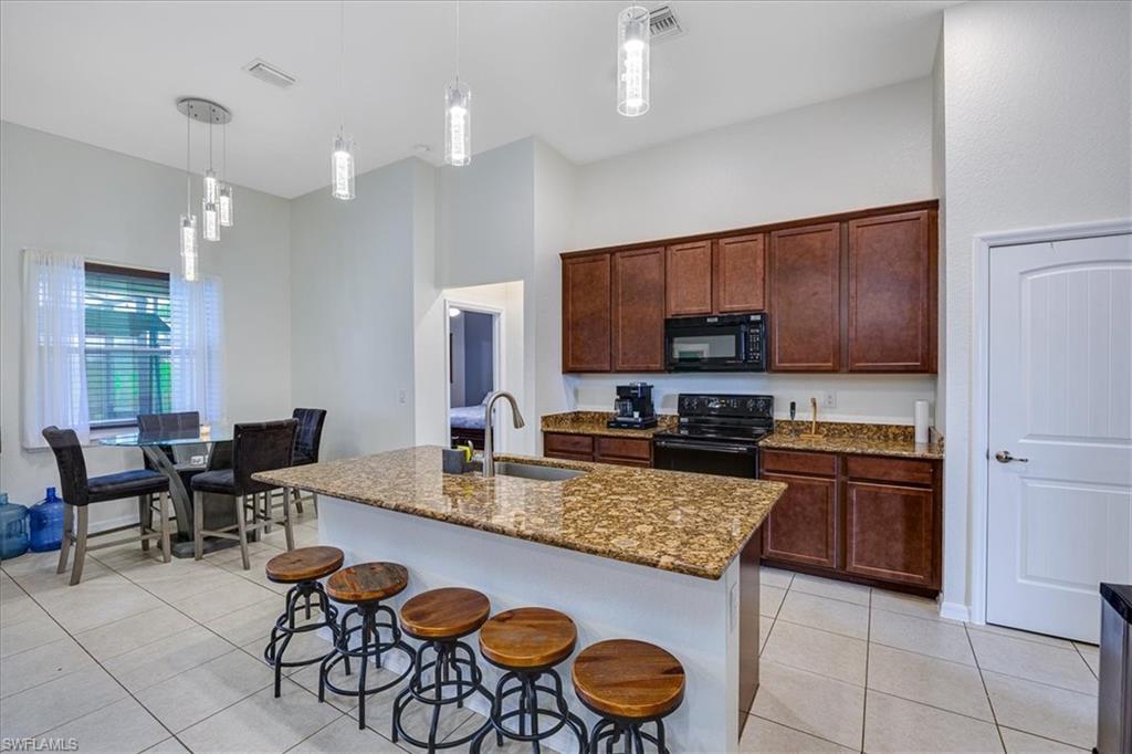 Kitchen featuring pendant lighting, black appliances, dark stone counters, and light tile patterned floors