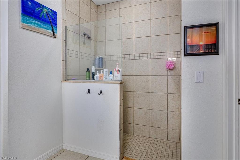 Mast. Bathroom featuring walk in shower, light tile patterned floors, and a textured wall