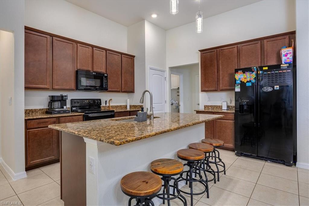 Kitchen with black appliances, a breakfast bar area, light tile patterned floors, dark stone countertops, and a high ceiling