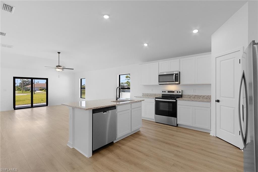 Kitchen featuring stainless steel appliances, light wood-style flooring, an island with sink, white cabinetry, and recessed lighting
