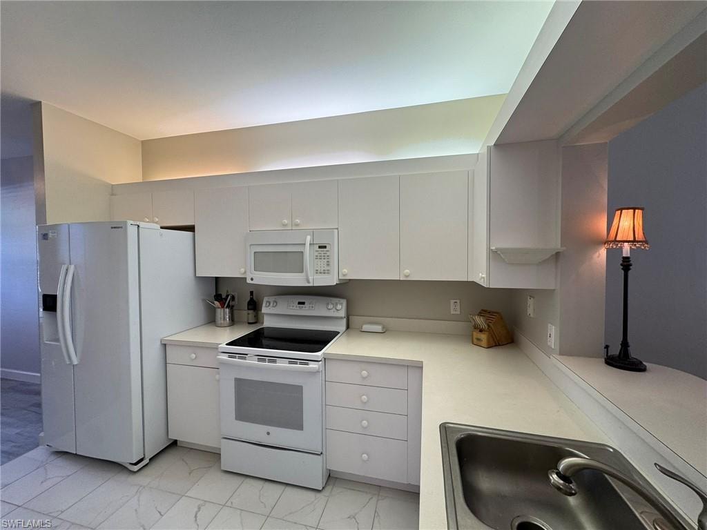 Kitchen with white cabinetry, sink, and white appliances