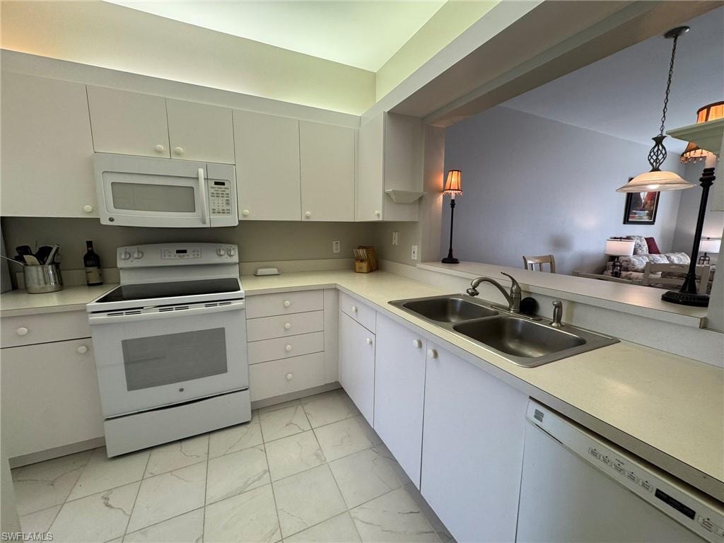 Kitchen with sink, white cabinets, hanging light fixtures, kitchen peninsula, and white appliances
