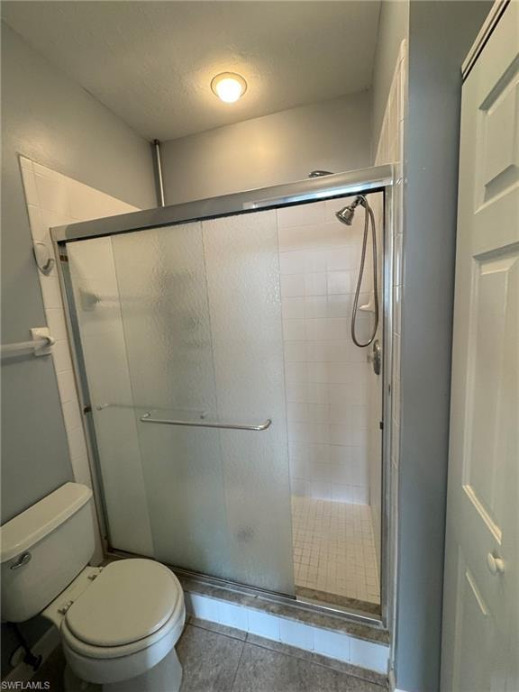 Bathroom with tile patterned floors, a shower with door, and toilet