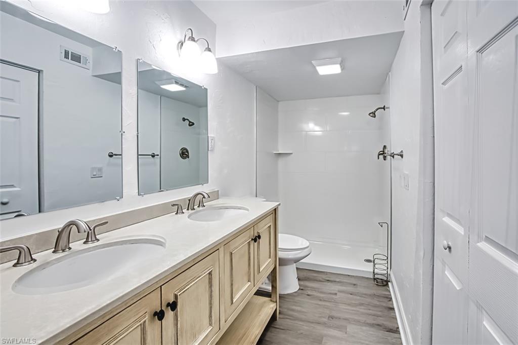 Bathroom featuring a stall shower, double vanity, and light wood-style flooring