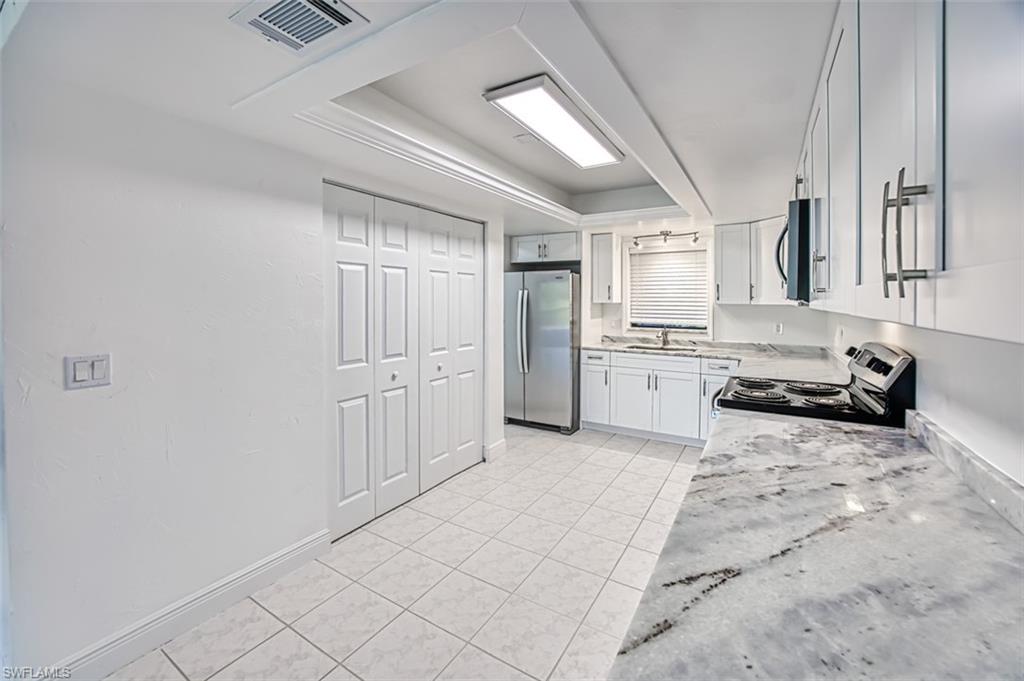 Kitchen featuring a raised ceiling, stainless steel appliances, white cabinetry, light tile patterned floors, and light stone counters
