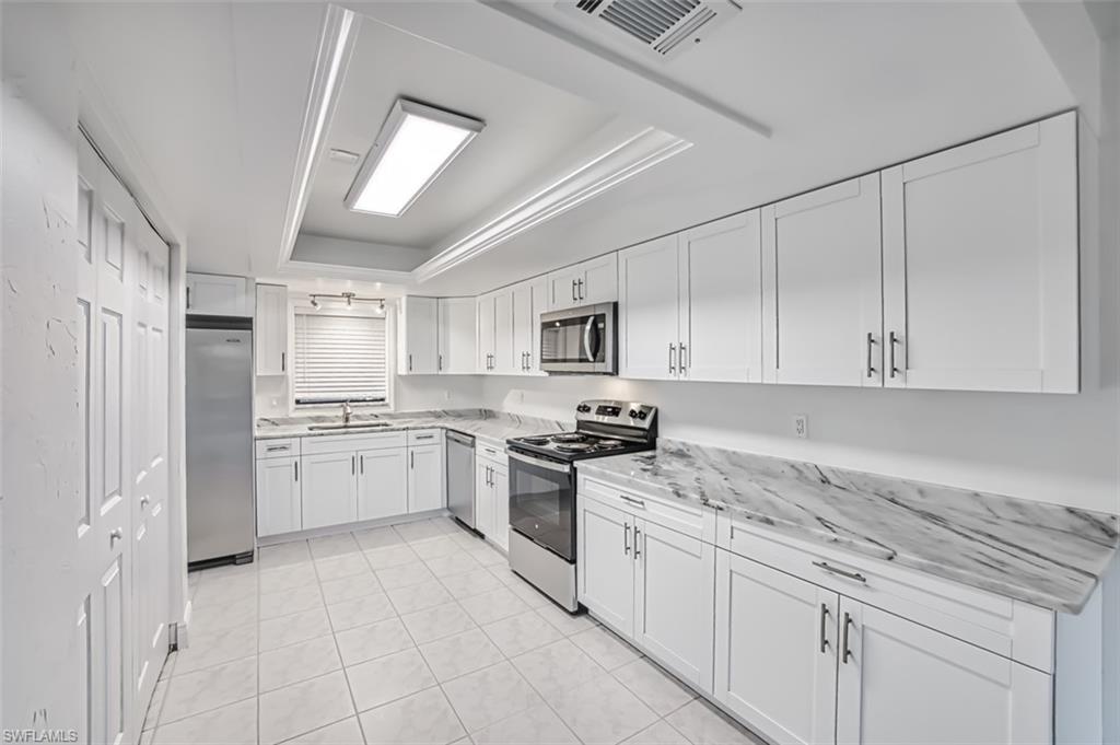Kitchen featuring a raised ceiling, stainless steel appliances, white cabinetry, light tile patterned floors, and light stone counters