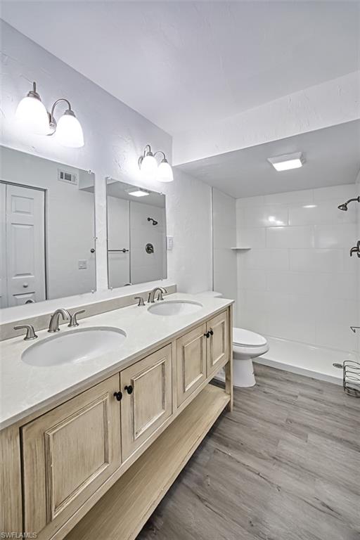 Full bathroom featuring a tile shower, double vanity, and light wood-style flooring