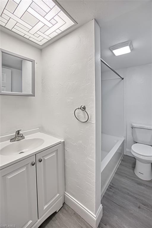 Bathroom with light wood-style flooring, vanity, shower / tub combination, and a textured wall